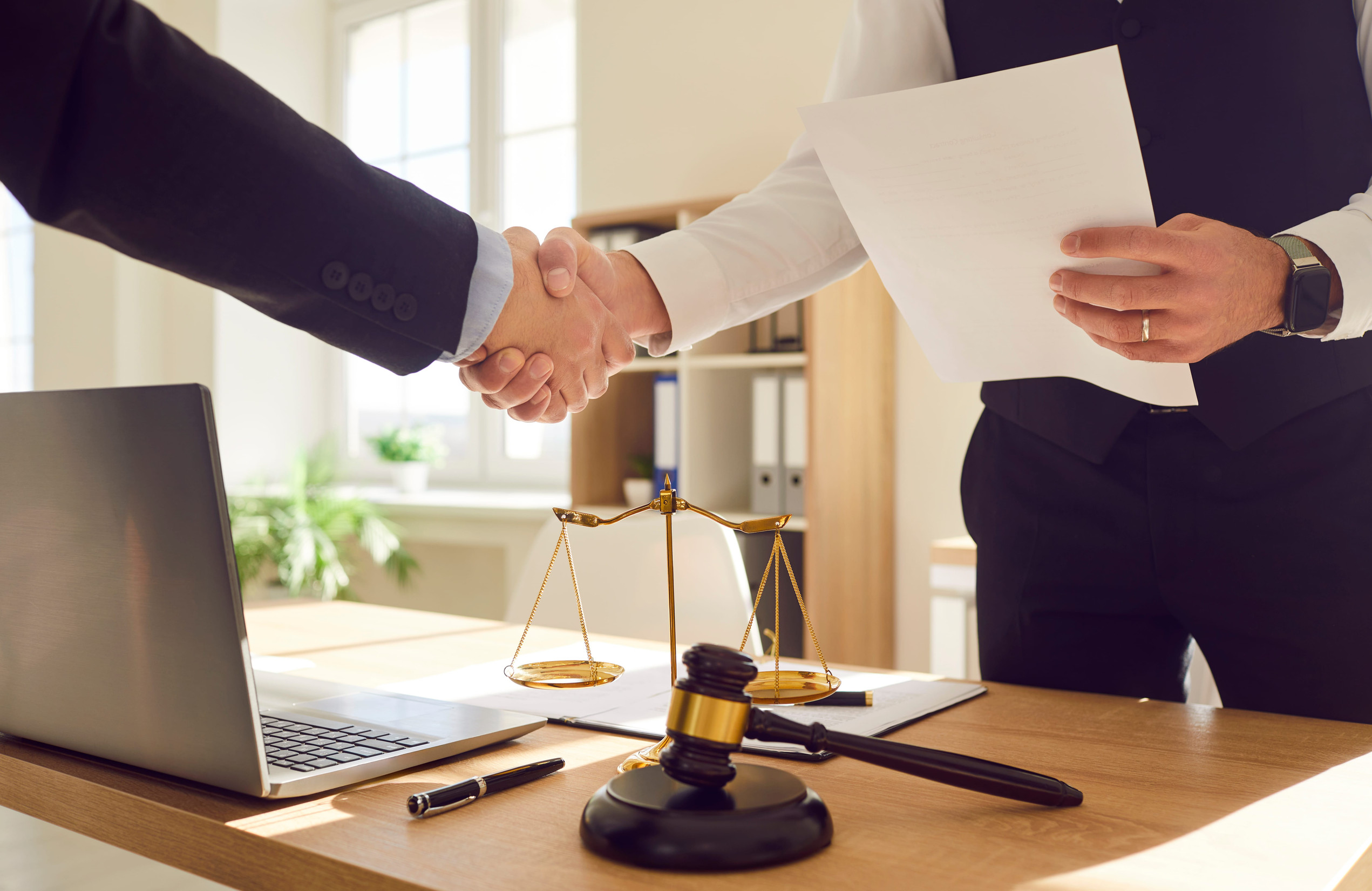 Cropped photo of a male lawyer working in office shaking hand with a man client standing at the desk on workplace with a laptop